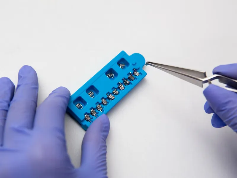 Orthodontist's gloved hands holding metal brace system and orthodontic instruments used for braces treatment in Sarjapura, Bangalore